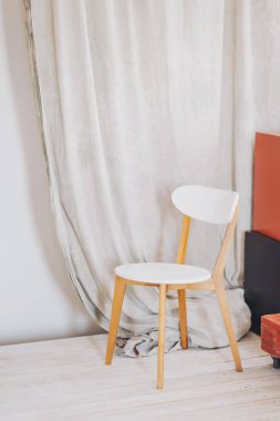 Zarif, minimalist bir köşe. Parlak, beyaz bir sandalye ve rahat bir iç mekan ortamında yumuşak kumaş örtüsü. Gündüz saatlerinde.