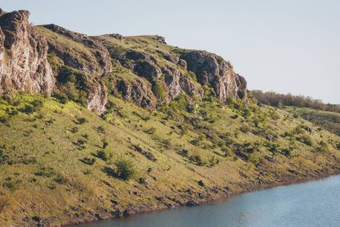 Doğanın dinginliği, yemyeşil ve kayalık çıkıntılarla dolu güneşli bir arazide sakin bir nehir kıyısı boyunca yankılandı.