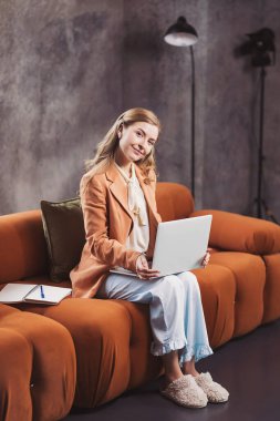 Freelancer, verimli bir günde rahat bir kanepede rahat bir ortamda çalışırken ilham buluyor. Evden çalışan, iş ceketli, pijama pantolonlu ve terlikli bir kadın.