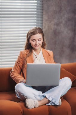 Freelancer, verimli bir günde rahat bir kanepede rahat bir ortamda çalışırken ilham buluyor. Evden çalışan, iş ceketli, pijama pantolonlu ve terlikli bir kadın.