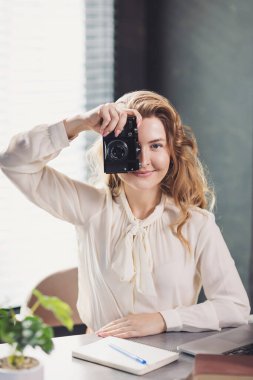 Freelancer, üretken bir çalışma sırasında şık bir ofis ortamında kamerayla anları yakalıyor. Genç bir serbest çalışan, şık ev ofisinde kamerasını tutarken gülümsüyor..