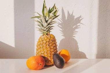 Pencere kenarındaki ahşap bir tabakta ananas, portakal, avokado ve elma içeren taze meyve düzenlemesi. Sıcak ortam sağlıklı yemek için mükemmel..