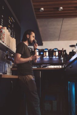 Barista, hareketli bir şehirde sıcak bir kafede kahve hazırlarken bir anlık düşüncelere dalmaktan zevk alır.