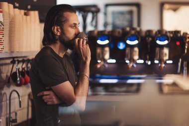 Barista, hareketli bir şehirde sıcak bir kafede kahve hazırlarken bir anlık düşüncelere dalmaktan zevk alır.