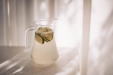 Taze limon dilimleri ve öğleden sonra ışığında yakalanan nane yapraklarıyla doldurulmuş ev yapımı limonata sürahisi.