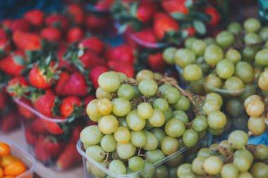 Yaz lezzetlerinin olgunlaşmış hasadı yerel çiftçi pazarında canlı kırmızı çileklerle dolu yeşil üzüm ve sepet kümelerine ev sahipliği yapıyor.