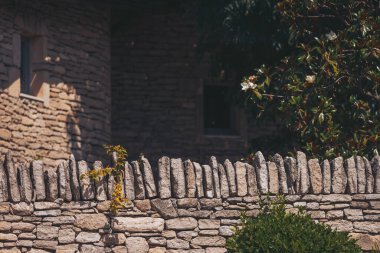 Eşsiz taş duvar sergileri, parlak öğleden sonra ışığı altında sakin bir kırsal alanda çiçek açan aksanlarla karışık tasarım sergiliyor.