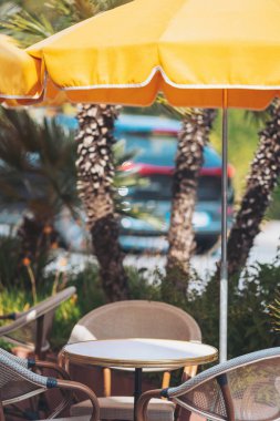 Güneşli bir günde, yemyeşil ve renkli manzaralarla çevrili sarı şemsiyeli canlı bir kafeterya.