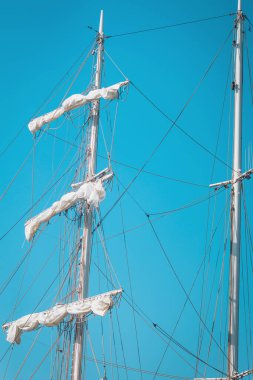 Uzun direkler parlak mavi gökyüzüne karşı yükselir, güneşli bir günde sakin bir güzellikte görkemli bir yelkenli gemisi sergiler