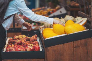 Gündüzleri kalabalık bir pazarda çeşitli ürünlerle dolu renkli ve canlı bir ortamda taze meyve seçen kişi