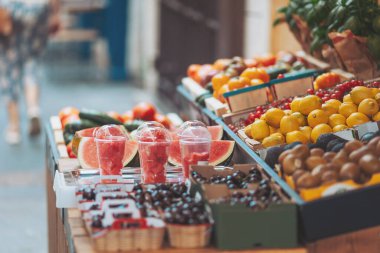 Canlı bir pazarda güneşli bir öğleden sonra, hareketli bir şehir bölgesinde taze meyve ve ferahlatıcı içecekler sergileniyor.