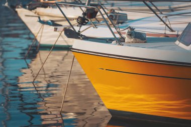 Gün doğumunda sakin bir limanda dizilen tekneler, durgun su yüzeylerinde canlı renkler ve yansımalar sergiliyor.
