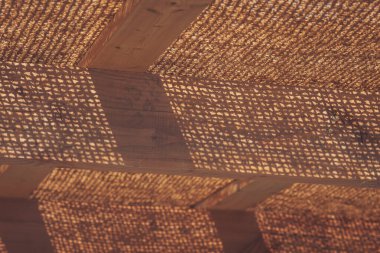 Örülmüş kumaştan süzülen güneş ışığı, öğleden sonra açık havada ahşap bir yüzey üzerinde karmaşık desenler oluşturur.