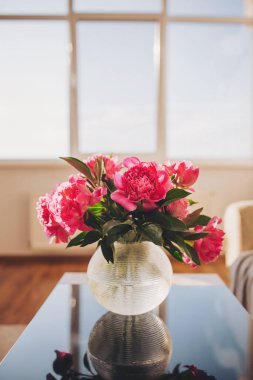 Canlı şakayıklar şık bir masada altın güneş ışığında güneşlenerek modern bir yaşam alanında sıcaklık ve dinginlik atmosferi yaratırlar.