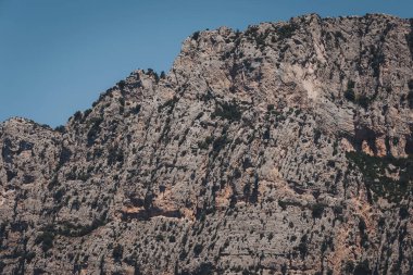 Görkemli kayalık kayalıklar, engebeli bir arazide berrak mavi bir gökyüzünün altında duruyor. Gün ortasında doğa oluşumlarının güzelliğini gözler önüne seriyor.