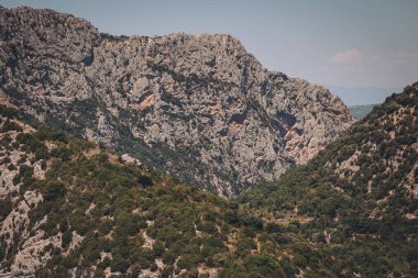 Görkemli kayalık kayalıklar, engebeli bir arazide berrak mavi bir gökyüzünün altında duruyor. Gün ortasında doğa oluşumlarının güzelliğini gözler önüne seriyor.