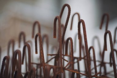 Paslı çelik çubuklar, sabahın erken saatlerinde bir inşaat sahasında bulanık bir arkaplan karşısında soyut bir desen oluşturuyor.