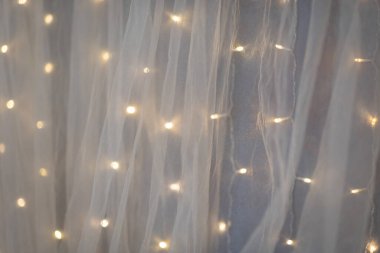 Hafifçe parlayan peri ışıkları alacakaranlıkta rahat bir odada narin beyaz bir perdeye karşı parıldar. Dinginlik ve yansıma için mükemmel sakin ve davetkar bir atmosfer yaratır.