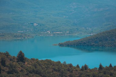Yelkenliler dingin turkuaz sularda, berrak mavi gökyüzünün altında berrak yeşil ağaçlarla çevrili sakin bir kıyı şeridinde huzur içinde sürüklenirler.