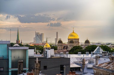 Riga 'nın tarihi çatılarının manzarası. Neo-Gotik bir bina ve karmaşık bir mimari. Görüntü uydu antenlerini, bacaları ve bulutlu gökyüzünün altında yemyeşil ağaçları yakalıyor..