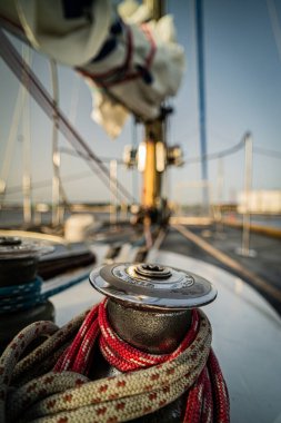 Renkli halatlarla sarılı yelkenli vincin detaylı bir yakın çekimi, gerekli yelken ekipmanlarını vurguluyor. Arka plandaki bulanık direk ve donanım denizcilik ayarını vurgular