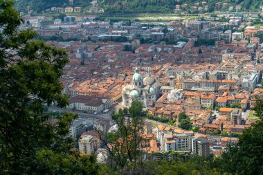 Terracotta çatıları, tarihi binalar ve yemyeşil yeşillikler çerçeveli modern yapılarla çevrili, belirgin yeşil kubbeleri olan bir Avrupa şehrinin panoramik görüntüsü..