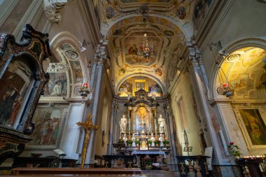 The ornate interior of a historic church featuring a decorated altar, religious paintings, frescoes, and intricate architectural details, illuminated by soft natural light and candlelight. clipart