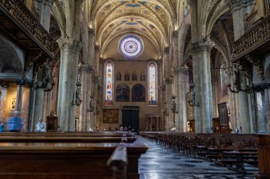 Büyük bir katedralin içi. Yükselen taş kolonlar, vitray pencereler ve karmaşık tavan. Ahşap sıralar boşluğu dolduruyor, dingin ve kutsal bir atmosfer yaratıyor..