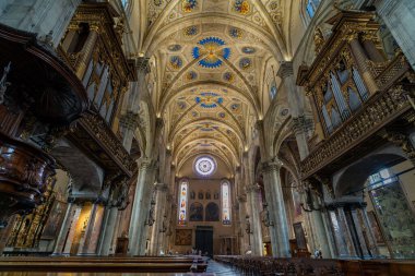 Büyük bir katedralin içi. Yükselen taş kolonlar, vitray pencereler ve karmaşık tavan. Ahşap sıralar boşluğu dolduruyor, dingin ve kutsal bir atmosfer yaratıyor..