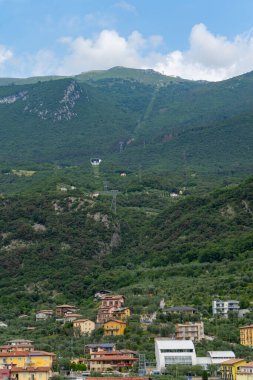 Etrafı yemyeşil yemyeşil, teleferik istasyonu ve dağların zirvelerine yükselen kablolarla çevrili, parçalı bulutlu bir gökyüzünün altında renkli yamaçlar..