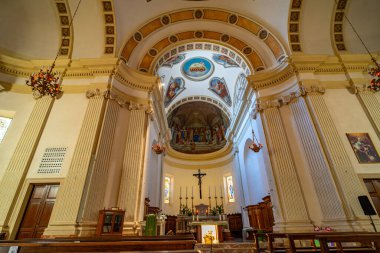 Tarihi bir kilisenin iç manzarası. Karmaşık mimari detaylar, büyük sütunlar ve süslü avizeler sergileniyor. Sunakta dini heykeller, mumlar yer alıyor.