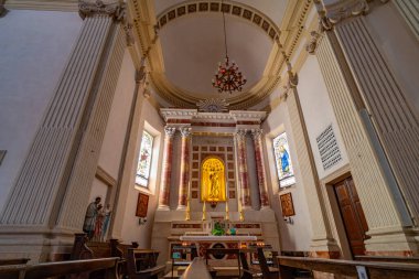 Interior view of a historic church showcasing intricate architectural details, grand columns, and ornate chandeliers. The altar features religious statues, candles clipart