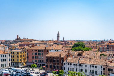 Venedik, İtalya 'nın panoramik manzarası, terracotta çatıları, tarihi binalar ve açık mavi gökyüzünün altındaki kilise kuleleri. Şehir manzarası Venedik mimarisi ve cazibesini ön plana çıkarıyor.