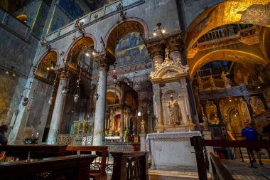 Altın mozaikler ve karmaşık freskler, yumuşak doğal ışık altında dini sanat ve mermer sütunların sergilendiği tarihi bir bazilikanın içini süslüyor..