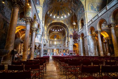 Altın mozaikler ve karmaşık freskler, yumuşak doğal ışık altında dini sanat ve mermer sütunların sergilendiği tarihi bir bazilikanın içini süslüyor..