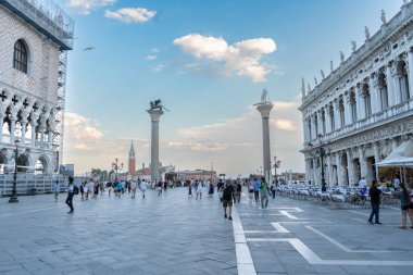 Saint Mark Meydanı, Venedik, İtalya 'da, San Marco ve San Todaro' nun iki tarihi sütununun yer aldığı, insanların yürüyüş yaptığı ve gezinti güvertesi boyunca açık kafelerin bulunduğu canlı bir sahne.