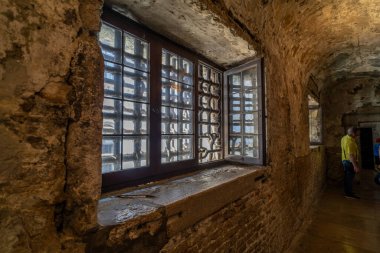 Karmaşık metal ızgaraları, kalın duvarları ve yaşlanmış, dokulu bir kapağı olan parmaklıklı pencerelerin yer aldığı loş ışıklı tarihi bir koridor..