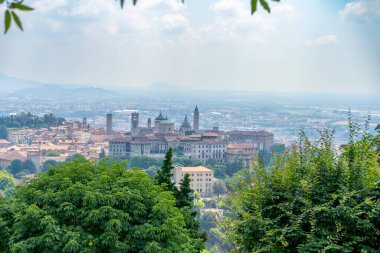 Ortaçağ kuleleri, kubbeli binaları ve sisli bir gökyüzünün altındaki yeşillikleri olan tarihi bir şehir..