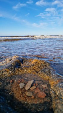 Yumuşak akşam ışığı büyük bir kayayı ve kumsalda çevreleyen çakıl taşlarını yıkıyor..