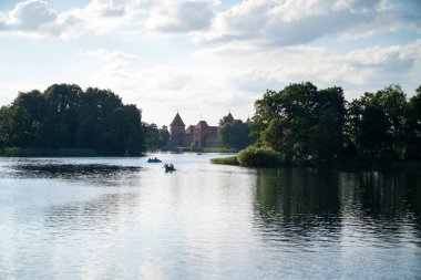 Sakin bir göl manzarası. İnsanlar sakin bir şekilde kayık kullanıyor. Gökyüzünün altında bir kale arkaplanı var..
