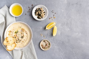Gri seramik tabakta zeytinyağlı humus. Atıştırmalık ekmek ve tost çubukları. Gri arkaplandaki üst manzara. Yüksek kalite fotoğraf