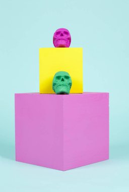 Pembe ve sarı küplerde parlak renkli plastik kafatasları. Cadılar Bayramı için neşeli ve sıradışı bir beste. En düşük renk hala yaşam fotoğrafçılığı.