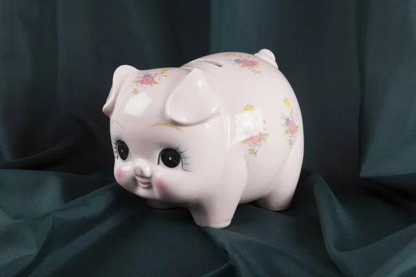 a vintage piggy bank in pink with flower designs on a wavy green curtain background. cute. Minimal color still life photography.