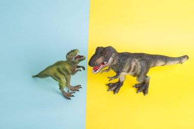 Ukrayna bayrağı metaforu gibi sarı ve mavi arka planda savaşan iki dinozor. Asgari natürmort ve renkli fotoğrafçılık