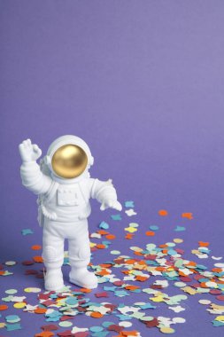 Uzay elbisesi giymiş bir astronot figürü konfeti halısında sade bir mor arka planı keşfediyor. Asgari yaratıcı natürmort fotoğrafçılık