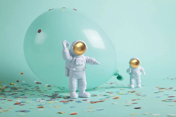 a cosmonaut couple exploring a new planet. They are surrounded by confetti and balloons. The whole is monochrome turquoise. Minimalist, trendy still life photography.
