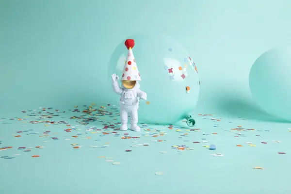 a cosmonaut couple exploring a new planet. They are surrounded by confetti and balloons. The whole is monochrome turquoise. Minimalist, trendy still life photography.