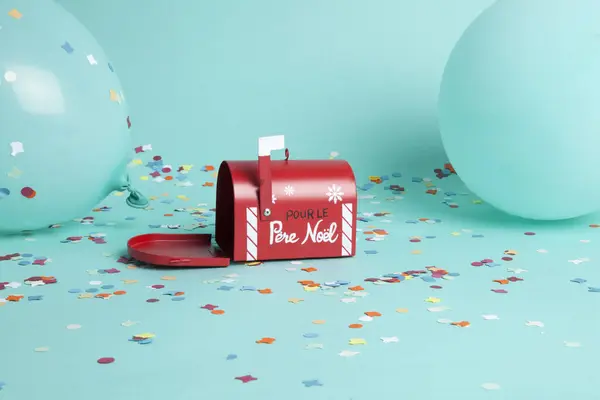 Santa\'s famous letterbox surrounded by confetti and balloons in the same turquoise color as the background. Written in French. Color harmony. Minimalist, trendy still life photography.