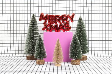 Parlak kırmızı bir Noel süsü. İçinde mutlu Noeller ve küçük Noel ağaçlarından oluşan minyatür bir orman sahnesi ve siyah beyaz grafikli sarı bir küpten oluşan bir metin var. En az natürmort