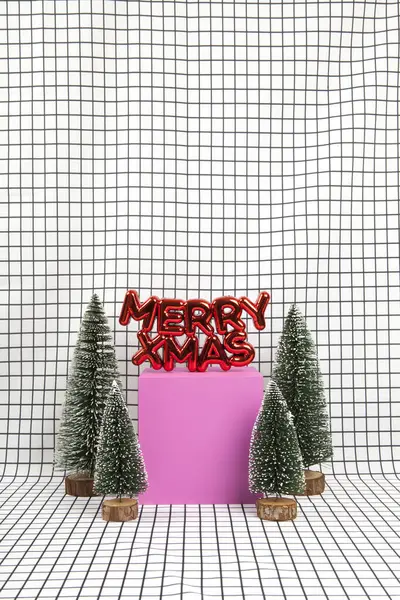 圣诞装饰品一种光滑的红色塑料圣诞装饰品 上面有一段文字写着圣诞快乐 还有一个由几棵小圣诞树和一个黄色立方体组成的小森林场景 其背景是黑色和白色的图形网格 最低限度的静物摄影 — 图库照片